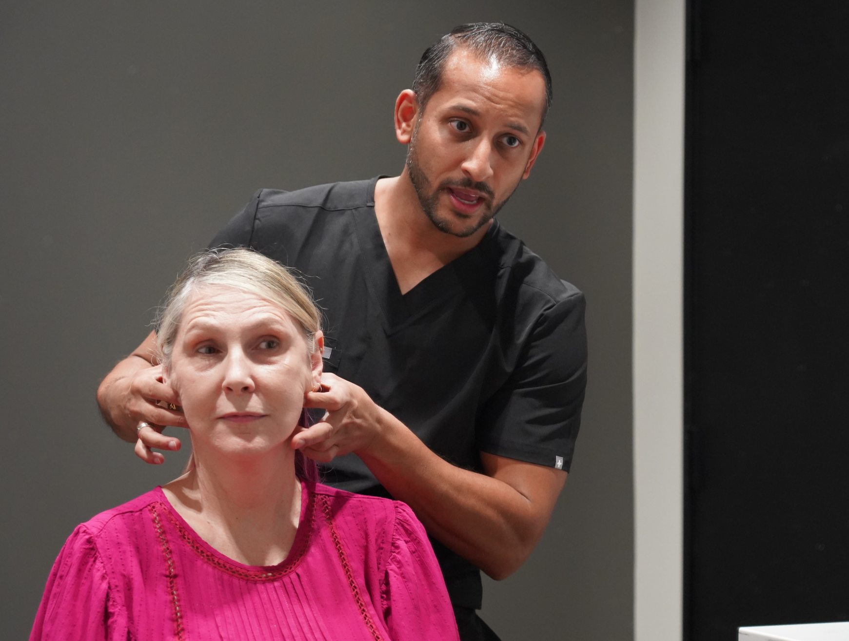 Dr. Patel demonstrating facial skin laxity on a patient during a facelift consultation in Dallas-Fort Worth, TX